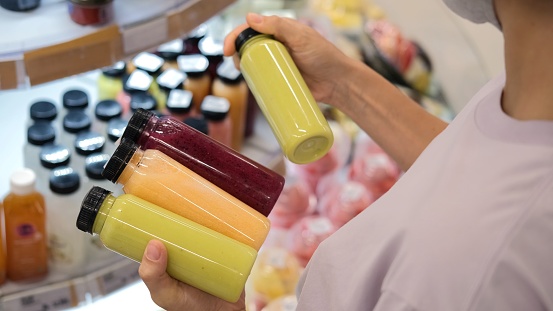 A woman customer in a store chooses bottles of freshly squeezed juice from different fruits and vegetables. Juice in plastic bottles of different colors, filled with vitamins from plants.