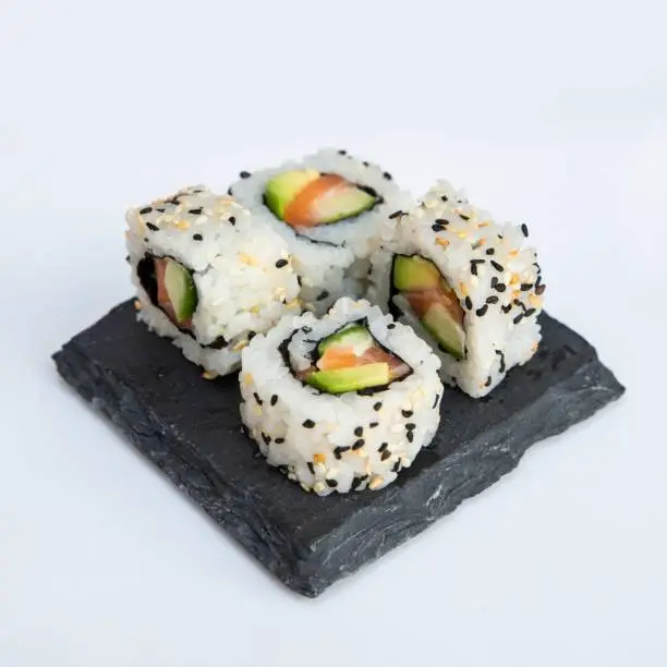Traditional delicious fresh sushi roll set on black stone on white background. California roll with rice, crab meat cucumber, avocado.