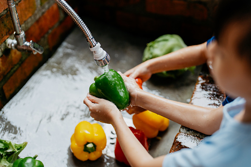 Image of an Asian boy and girls washing bell peppers and vegetables at kitchen sink