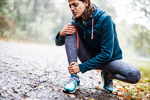 Young athletic woman feeling pain after injured her leg on sports training in autumn day. Copy space.