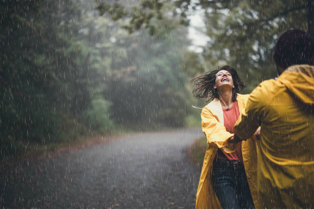 istock Happy couple in raincoats having fun while spinning on rain in nature. 1446186382