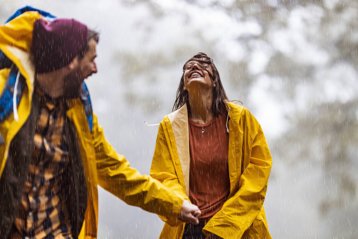 Cheerful woman holding hands with her boyfriend and having fun during rainy autumn day in nature.