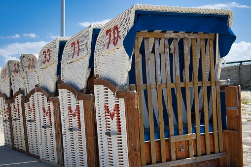A set of numbered beach basket chairs placed against each other under sunlight with blue cloudy sky above