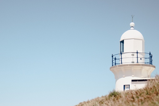A lighthouse behind a hill against a blue sky in Port Macquarie beach in Australia