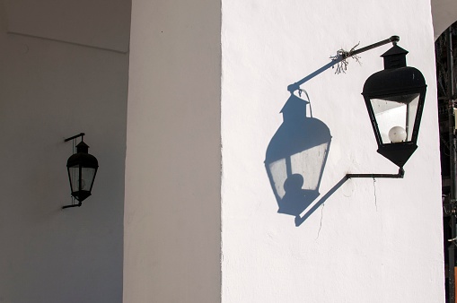 A closeup of a lamppost hanging on a white building with its shadow on a wall in Cabildo, Buenos Aires, Argentina
