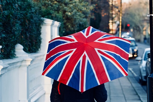 A back view of a walking person holding a British flag umbrella