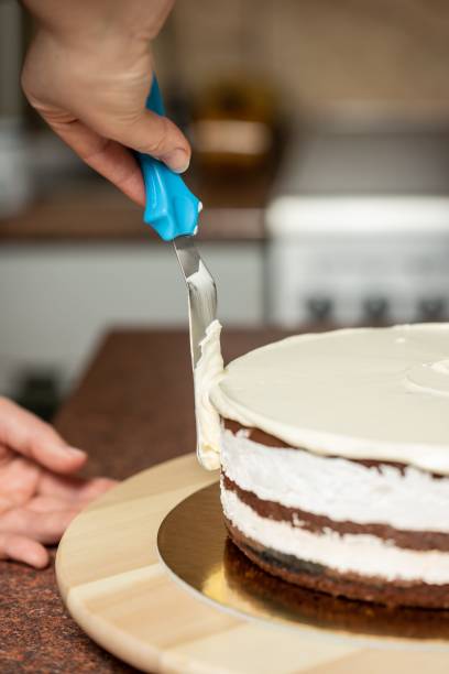 foto vertical de uma mulher alisando bordas de um bolo de chocolate com uma espátula, na cozinha - baking cake making women - fotografias e filmes do acervo