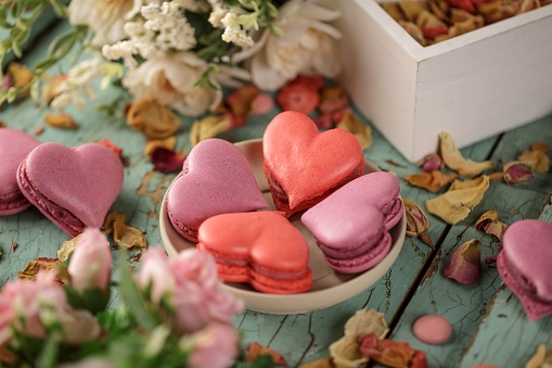 A closeup of heart shaped macarons on a blue wooden background surrounded by flowers