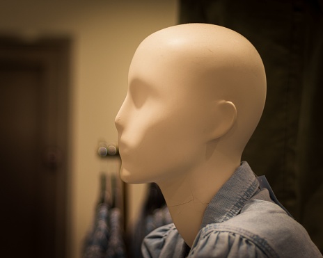 A closeup shot of a mannequin's head in a clothing shop with a blur background