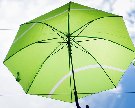 A closeup low-angle shot of a green umbrella stuck in between two wires under a blur cloudy sky background