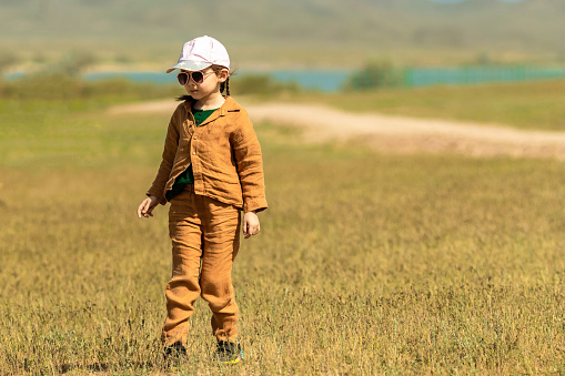 Little girl 5 years old outdoors in a dry sunny climate in the steppe in muslin clothes, a baseball cap and sunglasses.