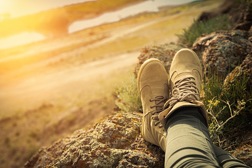 High laced hiking brown shoes on female legs in rocky terrain safari style. Copy space.