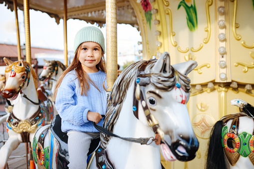 Adorable little girl on the playground. Toddler having fun on vintage carousel. Outdoor activities for small kids