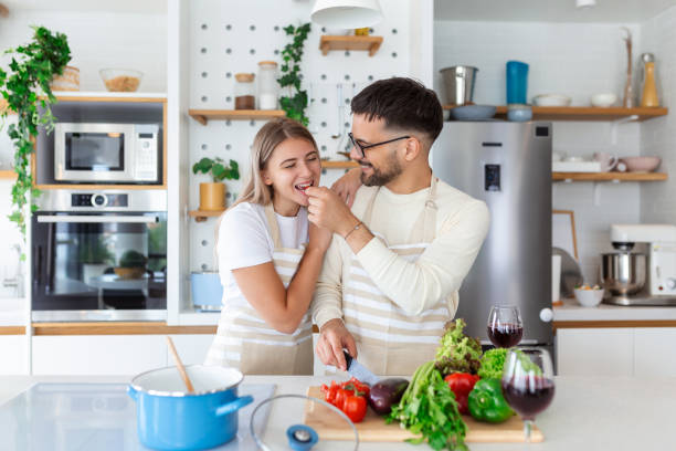 istock Beautiful young couple is looking at each other and feeding each other with smiles while cooking in kitchen at home. Loving joyful young couple embracing and cooking together, having fun in the kitchen 1446204248