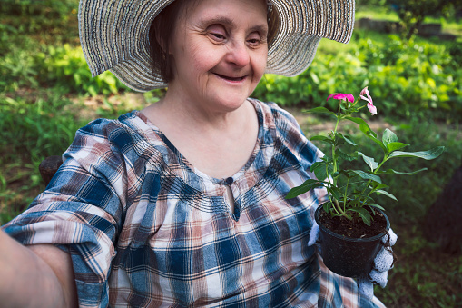 Happy woman with Down Syndrome ready to planting flowers. Gardening.