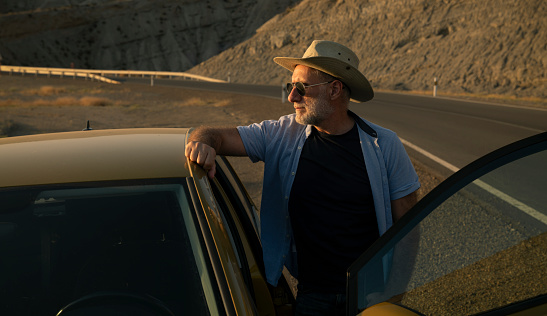 Adult man in cowboy hat and sunglasses standing against car in desert. Almeria, Spain