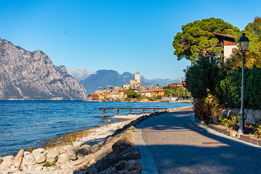 Lakeshore of Lake Garda (Lago di Garda) and the small Malcesine village with the castle. Verona province, Italy, Veneto, southern Europe. On background the coast of the Lombardy and Trentino-Alto Adige.