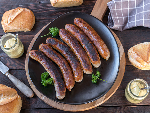 Traditional german meal with fried pork sausage or bratwurst with fresh buns and mustard. Served on rustic and dark wooden table background. Flat lay
