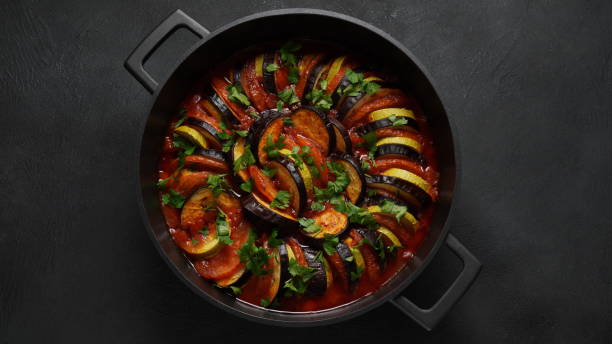 Layered ratatouille in a baking dish, slices of zucchini, red bell pepper, chili, yellow squash, eggplant, olive oil, parsley and garlic Layered ratatouille in a baking dish, slices of zucchini, red bell pepper, chili, yellow squash, eggplant, olive oil, parsley and garlic ratatouille stock pictures, royalty-free photos & images