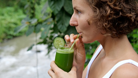A woman on vacation drinks a delicious smoothie of green vegetables and fruits with the addition of herbs and greens. Detox during rest to restore health and cleanse the body.