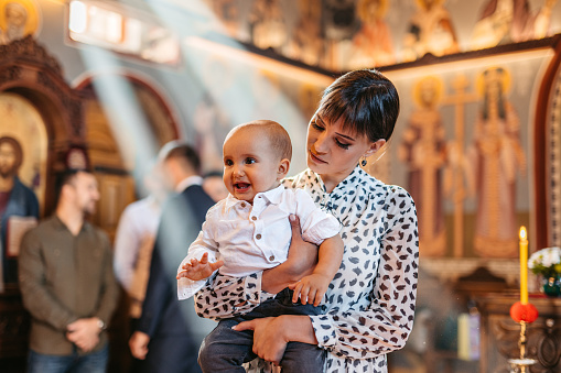 Young mother holding her baby boy during christening in an Orthodox church.