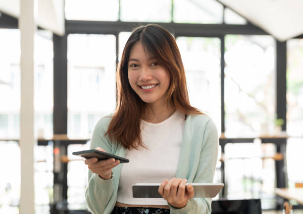 istock Young asian woman using mobile phone and digital tablet looking on camera 1446220743