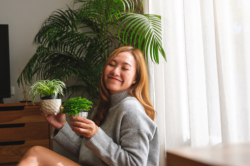Smiling woman in her 30s holding a pot with a plant on the balcony.