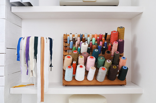 Wooden holder with collection of different threads on shelf in tailor studio