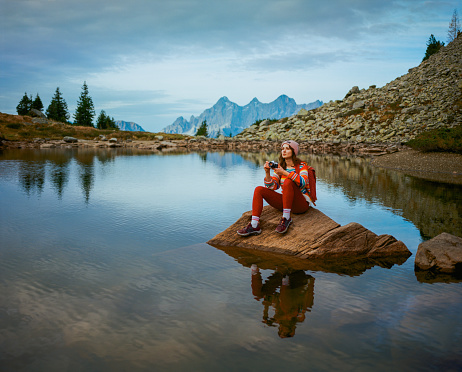 Young Caucasian woman with camera  sitting  on the background of lake in Austria