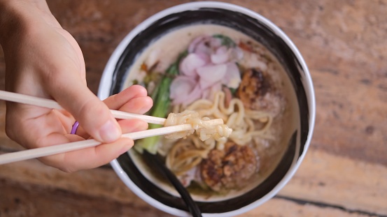 Popular Asian food ramen in the restaurant. Simple and delicious Asian noodles traditional food with vegetables and meat. Ramon noodles are eaten using chopsticks in a street restaurant.