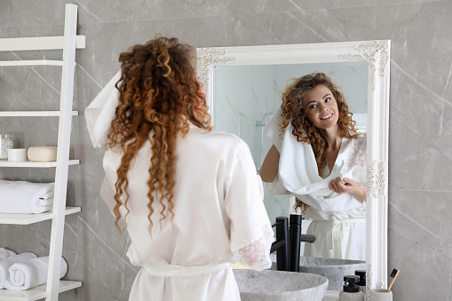 Beautiful woman drying hair with towel near mirror in bathroom