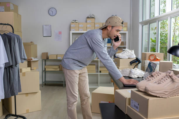 istock Asian man e-commerce business owner using phone and looking at laptop in store warehouse. 1446232372