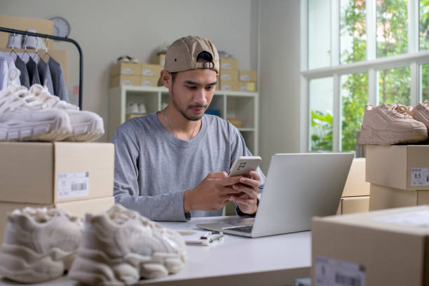 istock Asian man e-commerce business owner using smartphone and laptop in store warehouse. 1446232425