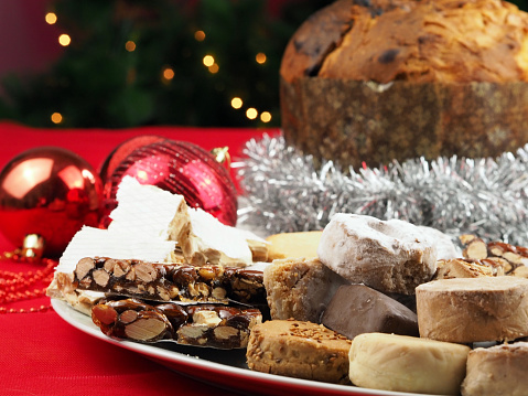 Traditional Mediterranean sweets: panettone, polvorones, mantecados, and turron. Against the background of the Christmas tree.