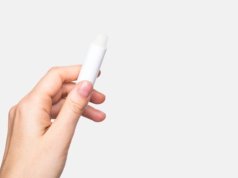Female hand holds hygienic moisturizing lipstick on gray background. lip care concept, copy space