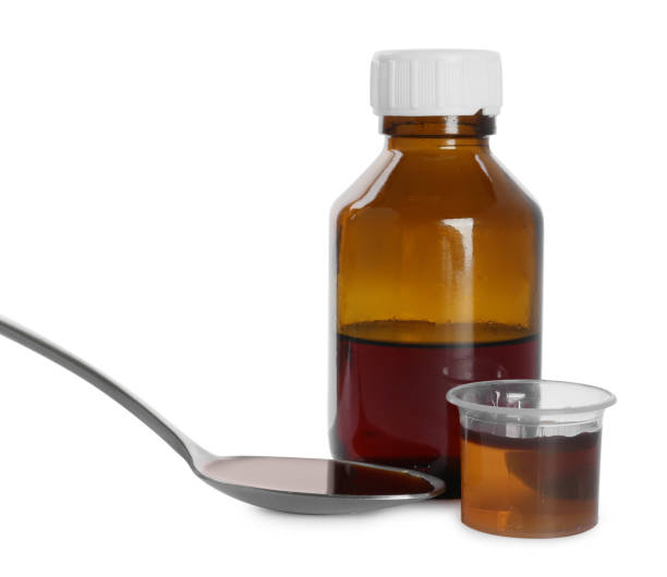 istock Bottle of cough syrup, spoon and measuring cup on white background 1446234169