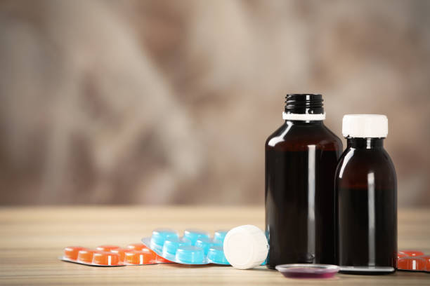 istock Bottles of syrup, dosing spoon and cough drops on wooden table. Space for text 1446234257