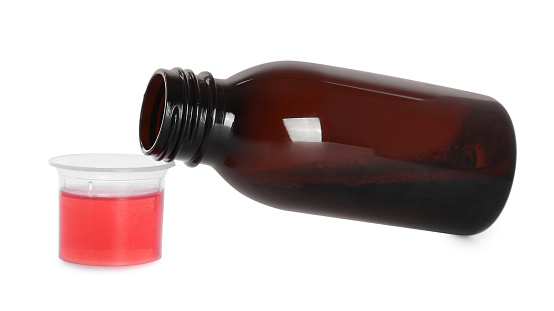 Bottle of cough syrup and measuring cup on white background