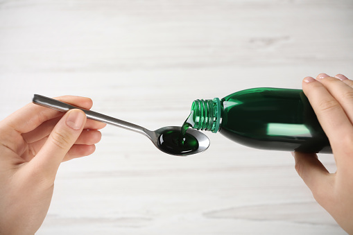 Woman pouring cough syrup into spoon on light background, closeup