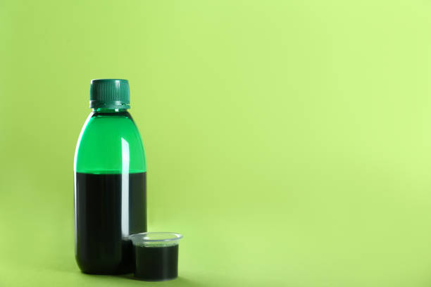 istock Bottle of cough syrup and measuring cup on light green background. Space for text 1446234573