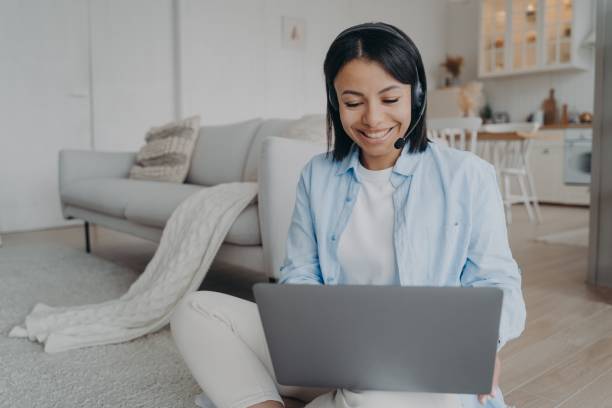 istock Smiling female coach in headset work on laptop or study online, sitting on floor at home. E-learning 1446235683