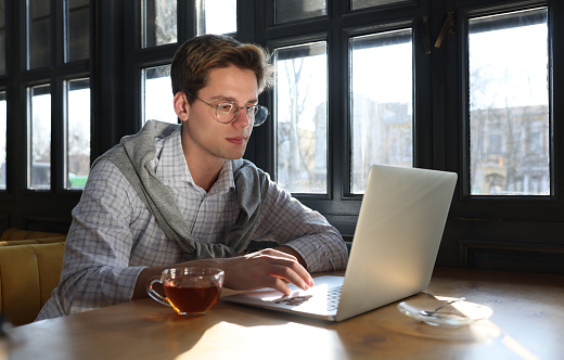 Teenage student with laptop studying at table in cafe