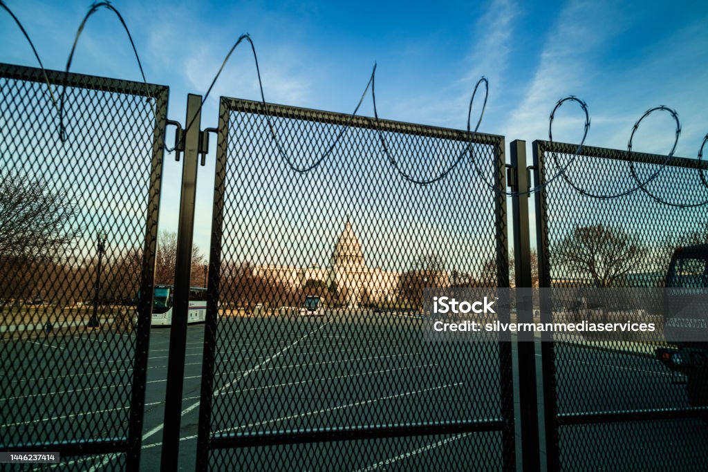 U.S. Capitol Building Behind Metal Fence with Razor Wire After January 6th Riot - Washington, D.C. The U.S. Capitol building at sunset, fortified behind a metal fence topped with razor wire to address security concerns in the months following the January 6th, 2021 insurrection. Washington, DC. Architectural Dome Stock Photo