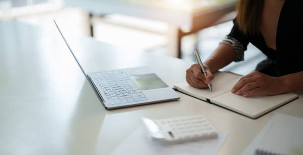 istock Cropped photo of woman writing making list taking notes in notepad working or learning on laptop indoors- educational course or training, seminar, education online concept 1446238688