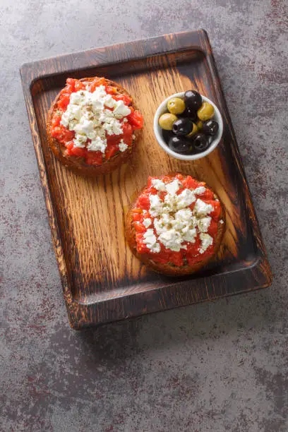 Dakos Cretan Meze appetizer with barley rusk, tomatoes, feta cheese, oregano and olive oil closeup on the wooden board on the table. Vertical top view from above