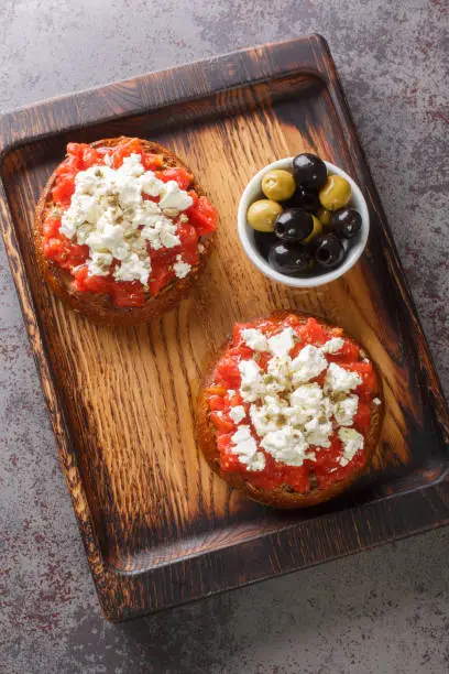 Traditional meze or a light meal on the island of Crete, dakos is often called Greek bruschetta closeup on the wooden board on the table. Vertical top view from above