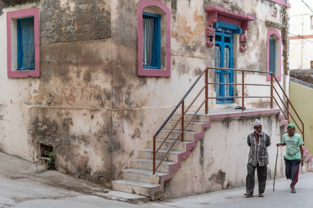 Two old men walking past an old Portuguese era house Diu, India - December 2018: Two old men walking past an old Portuguese era house in the streets of Diu. diu island stock pictures, royalty-free photos & images