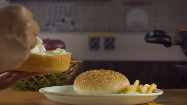 Female spreading mayonnaise on a burger bun slice with a spoon - making a burger, fast food preparation