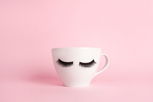 White cup coffee or tea mug with false lashes on a pink background. Morning energy. Female cute background