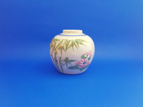 A small ceramic urn for indoor decoration with a white base color combined with relief ornaments on the outside, isolated on a blue background